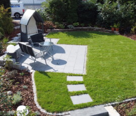 Professionelle Gartengestaltung in Göttingen: Modern angelegte Terrasse mit Einfassungsmauer, perfekt gepflegtem Rollrasen und Rindenmulch-Beeten von Bandelow & Uhlendorff.
