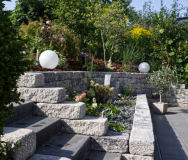 Hochwertige Gartengestaltung in Göttingen: Detailansicht einer modernen Steintreppe, eingefasst von hellen Steinmauern und einem bepflanzten Kiesbeet, realisiert von Bandelow & Uhlendorff.